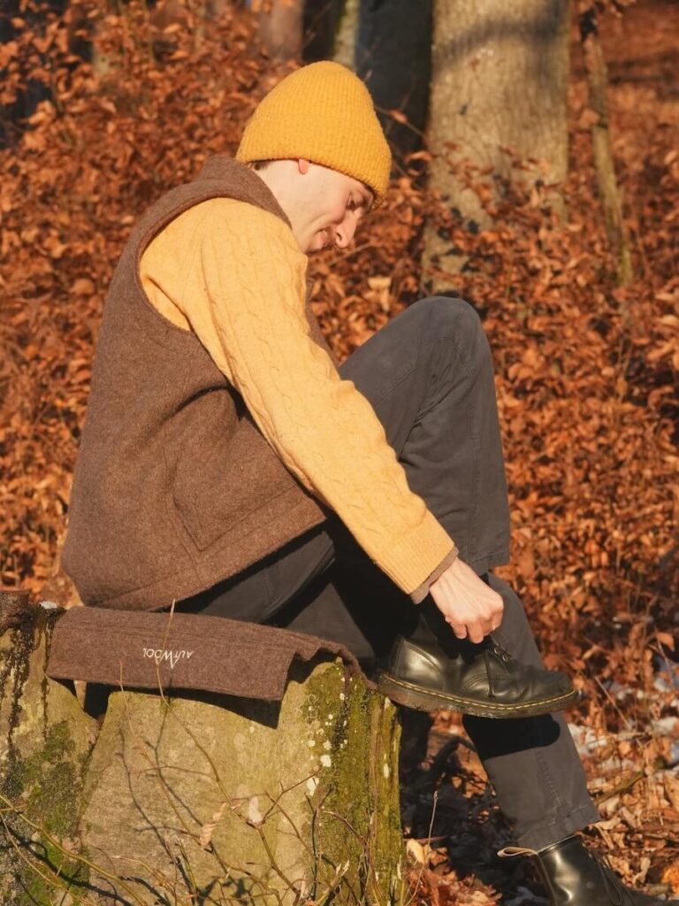 Junger Mann vor herbstlichem Hintergrund, bindet sich die Schuhe zu.